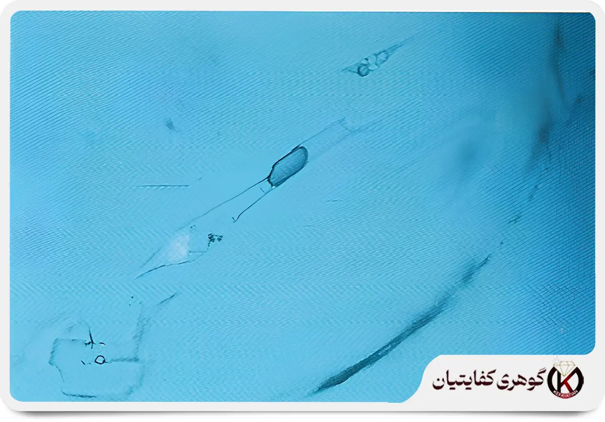 این تصویر میکروسکوپی، ناپاکی طبیعی و منحصر به فرد زمرد پنجشیر را به نمایش میگذارد. این ادخالهای چندفازی (حاوی مواد معدنی، مایع و گاز) که در دل سنگ تشکیل شدهاند